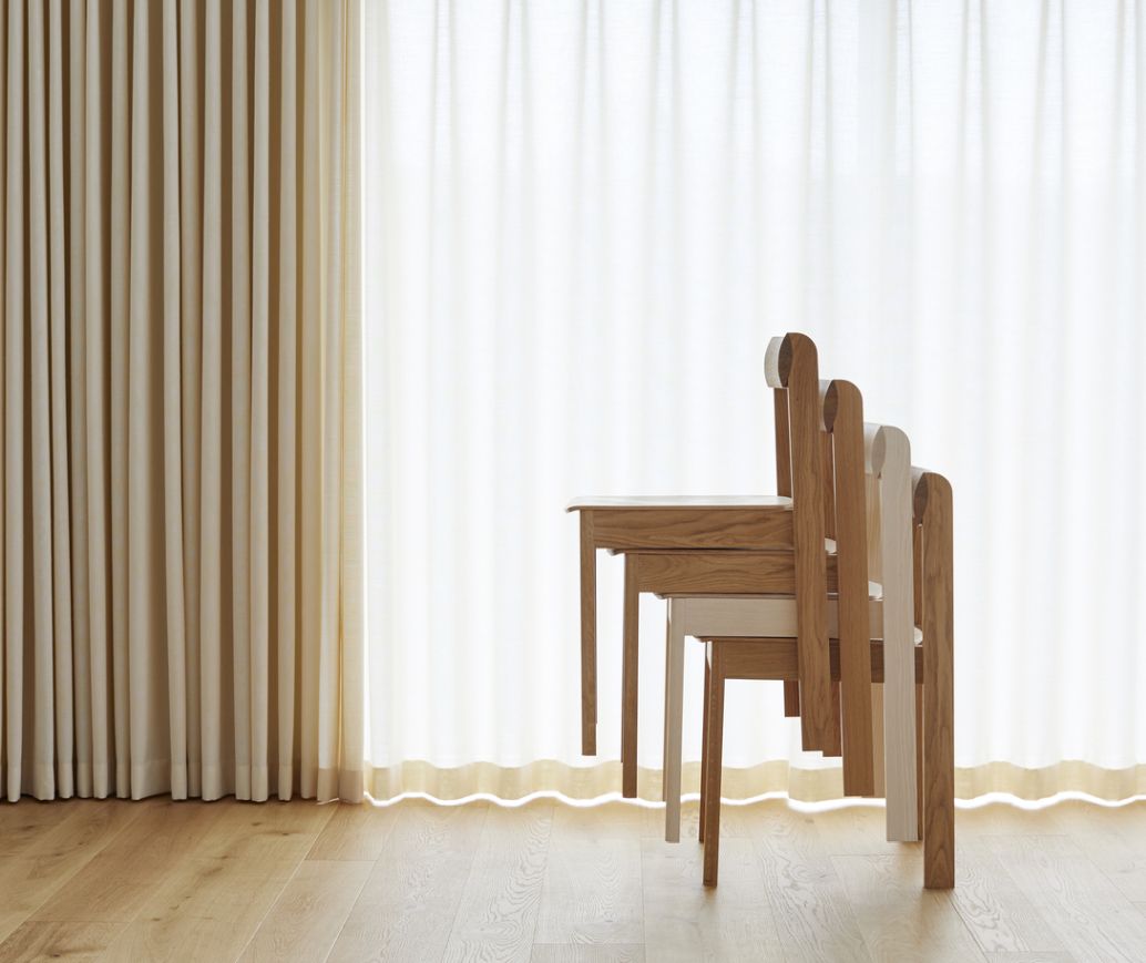 Stapelbare Holzstühle in verschiedenen Farben vor hellem Vorhang, modernes Möbeldesign für Esszimmer und Küche.