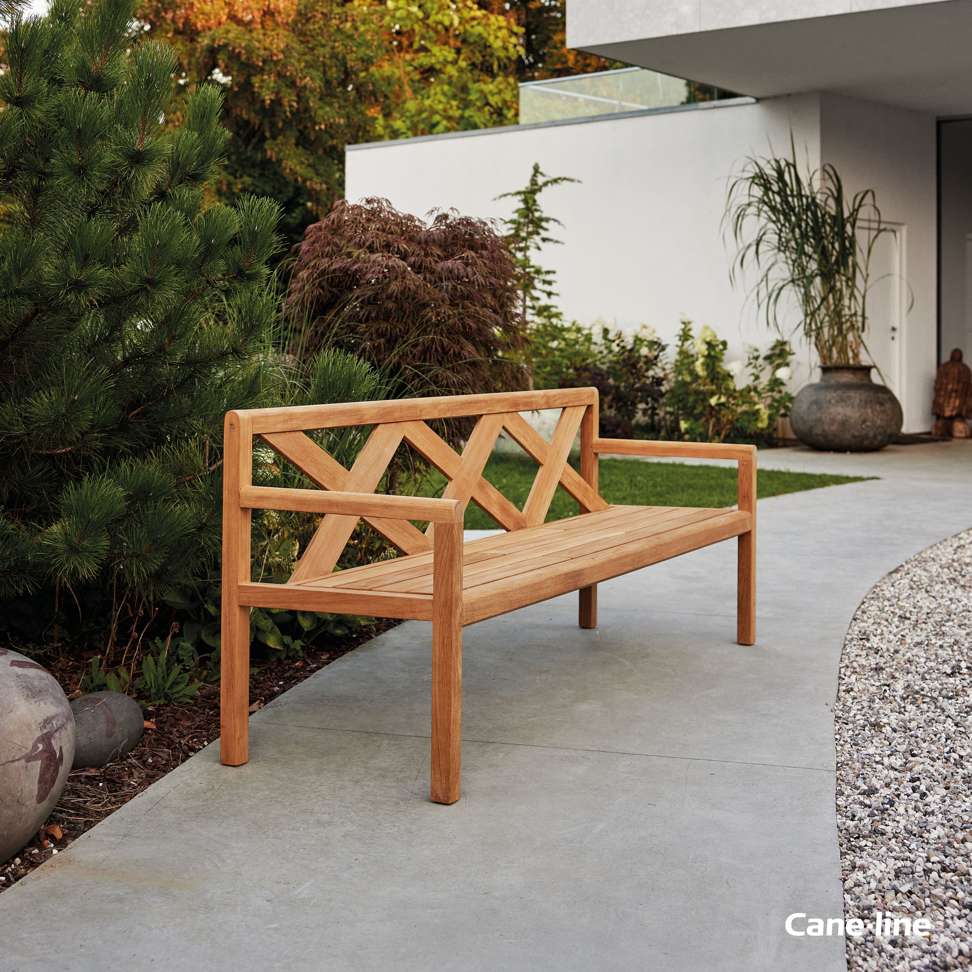 Grace Bank von Cane-Line: Gartenbank aus Teakholz mit Kreuzmuster vor modernem Haus.