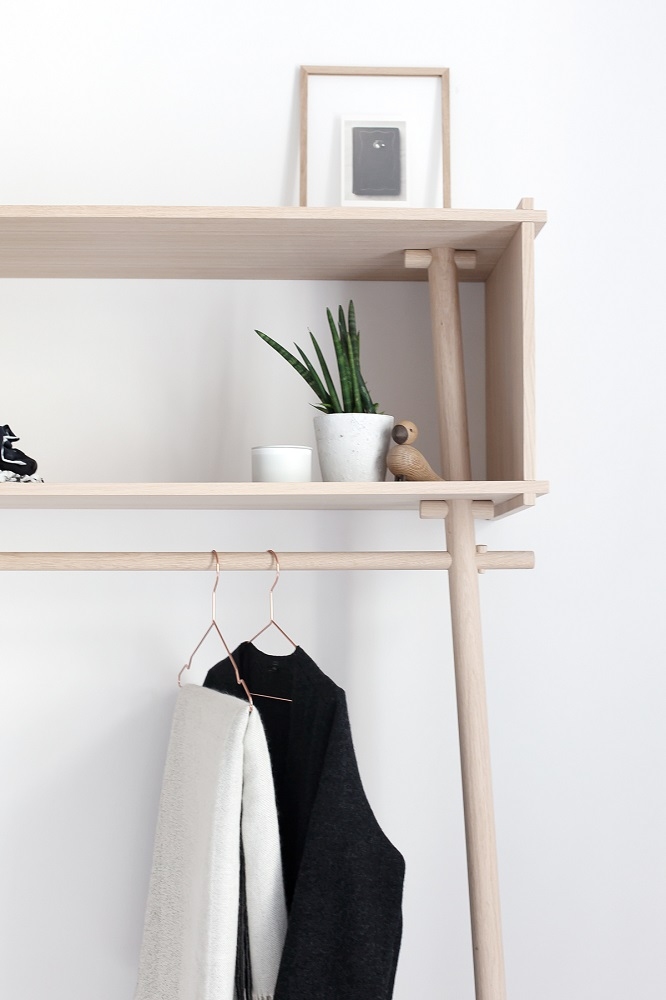 Töjbox Anlehngarderobe aus Eiche, weiß pigmentiert, mit Kleidung, Dekoration und Ablagefläche vor weißer Wand.