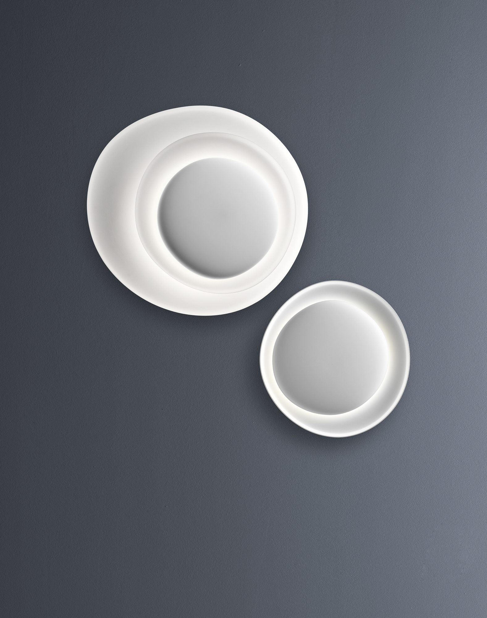 Weiße Bahia Wandleuchte von Foscarini mit LED-Beleuchtung an grauer Wand. Design Lampe.