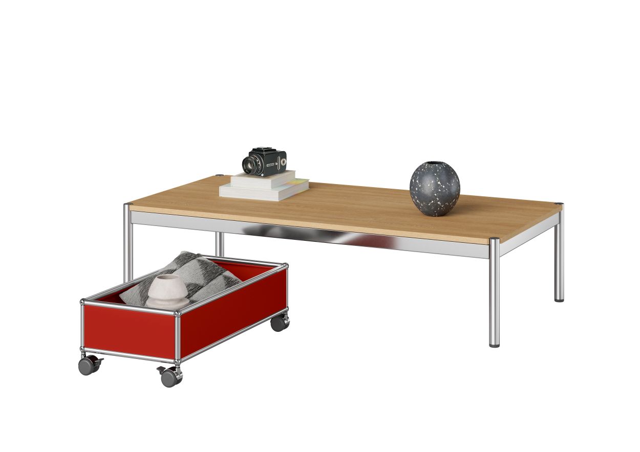 USM Haller Tisch mit roter Rollbox, hellbrauner Tischplatte und Deko-Elementen auf weißem Hintergrund.