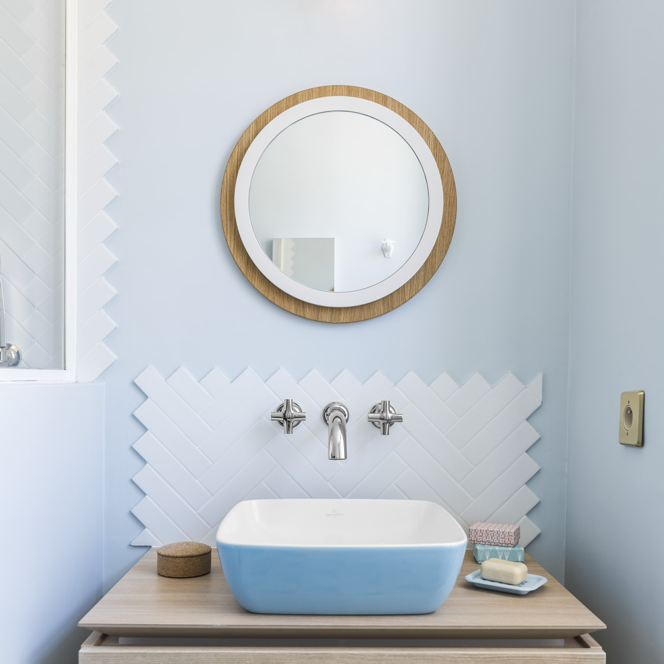 Badezimmer mit blauem Waschbecken und rundem Back to Bauhaus Spiegel mit Holzrahmen.