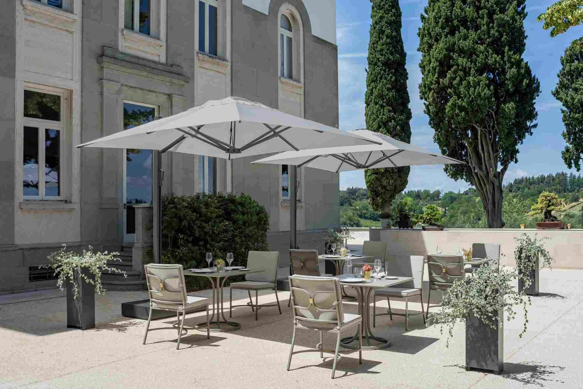 Emu Chari Stuhl Outdoor: Elegantes Gartenmöbel-Set mit Stühlen und Tischen unter Sonnenschirmen.