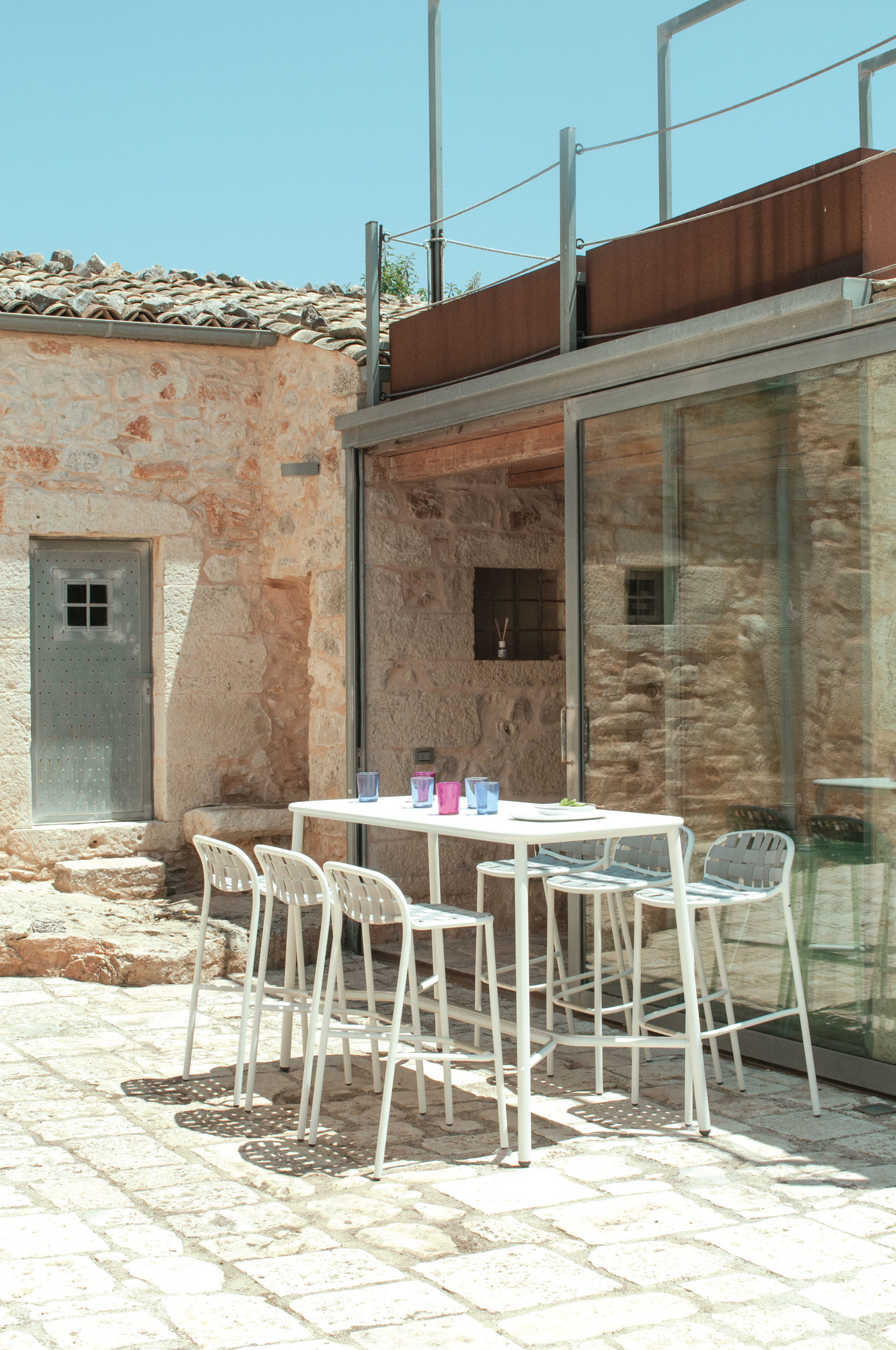 Yard Stehtisch von emu mit Barhockern im Außenbereich vor einem Gebäude aus Naturstein.