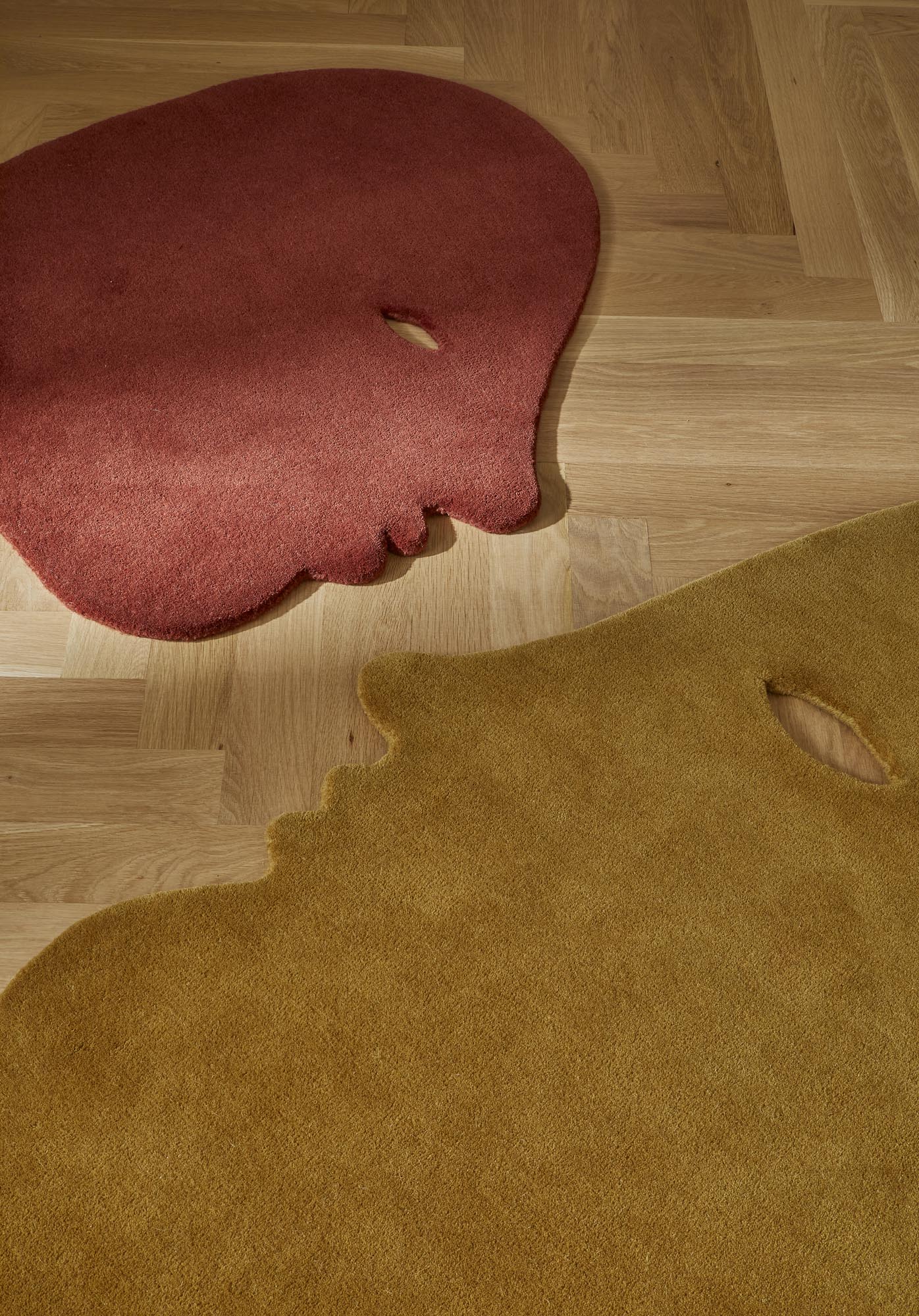 Detailaufnahme von zwei abstrakten, farbigen Teppichen der Marke Nanimarquina Talk Talk auf einem Holzboden.