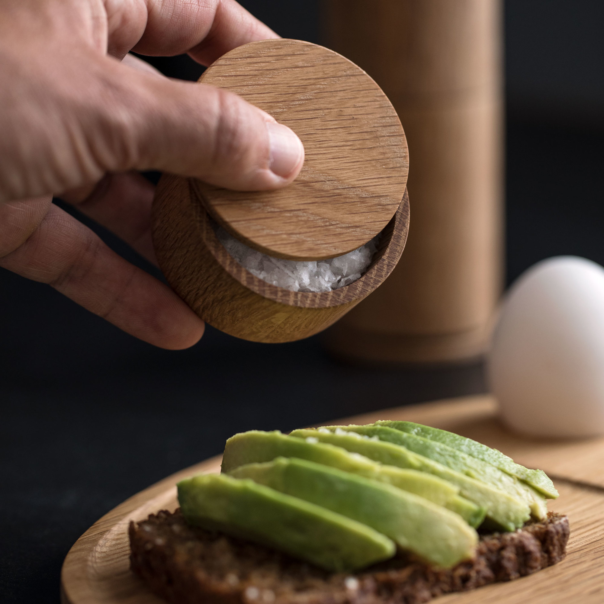 Salt Me Salzbehälter aus Holz wird über Avocado-Brot gehalten, um Essen zu würzen.