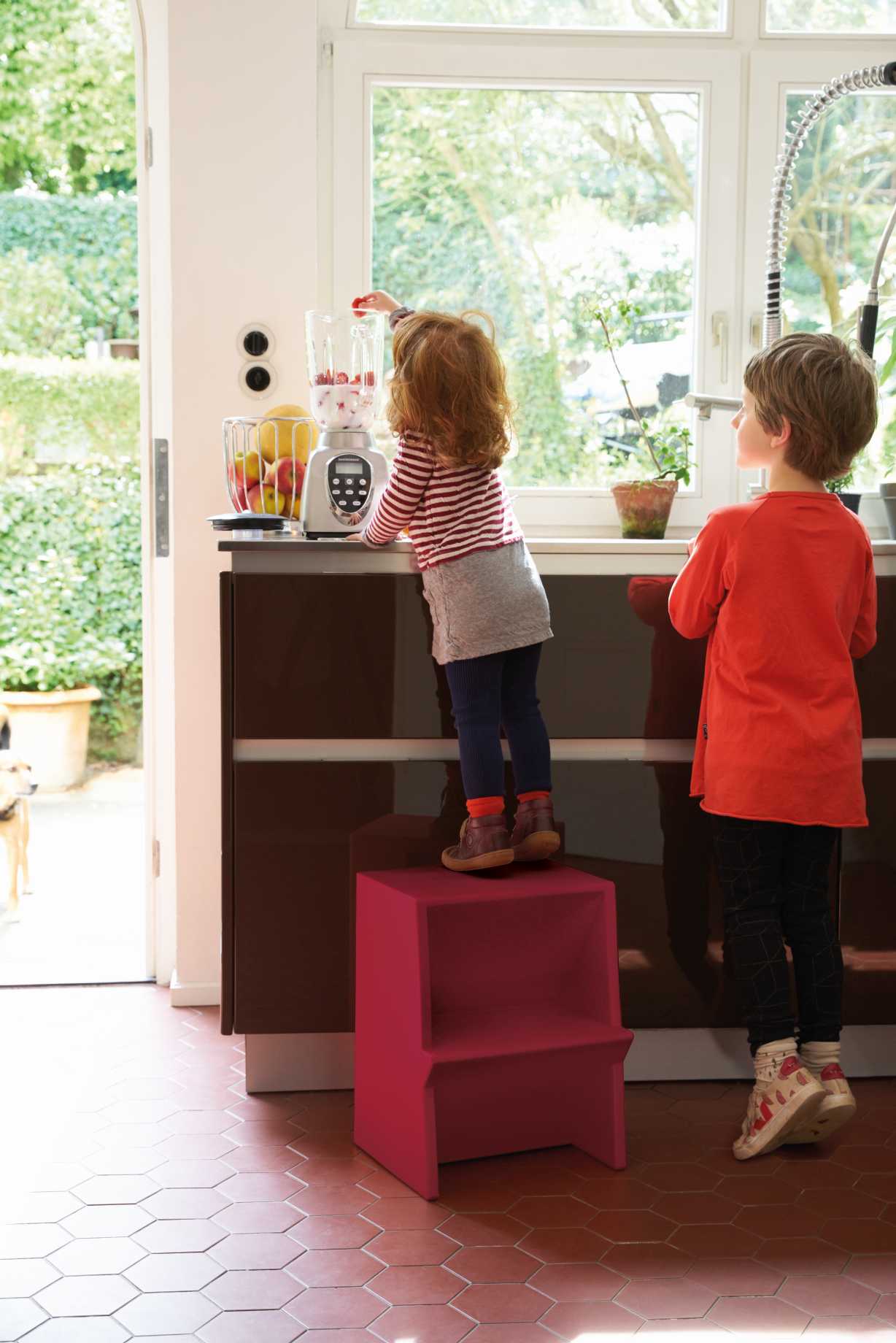 Kind auf hellgelbem Mono Tritthocker von Richard Lampert in Küche, um an Küchengerät zu gelangen.