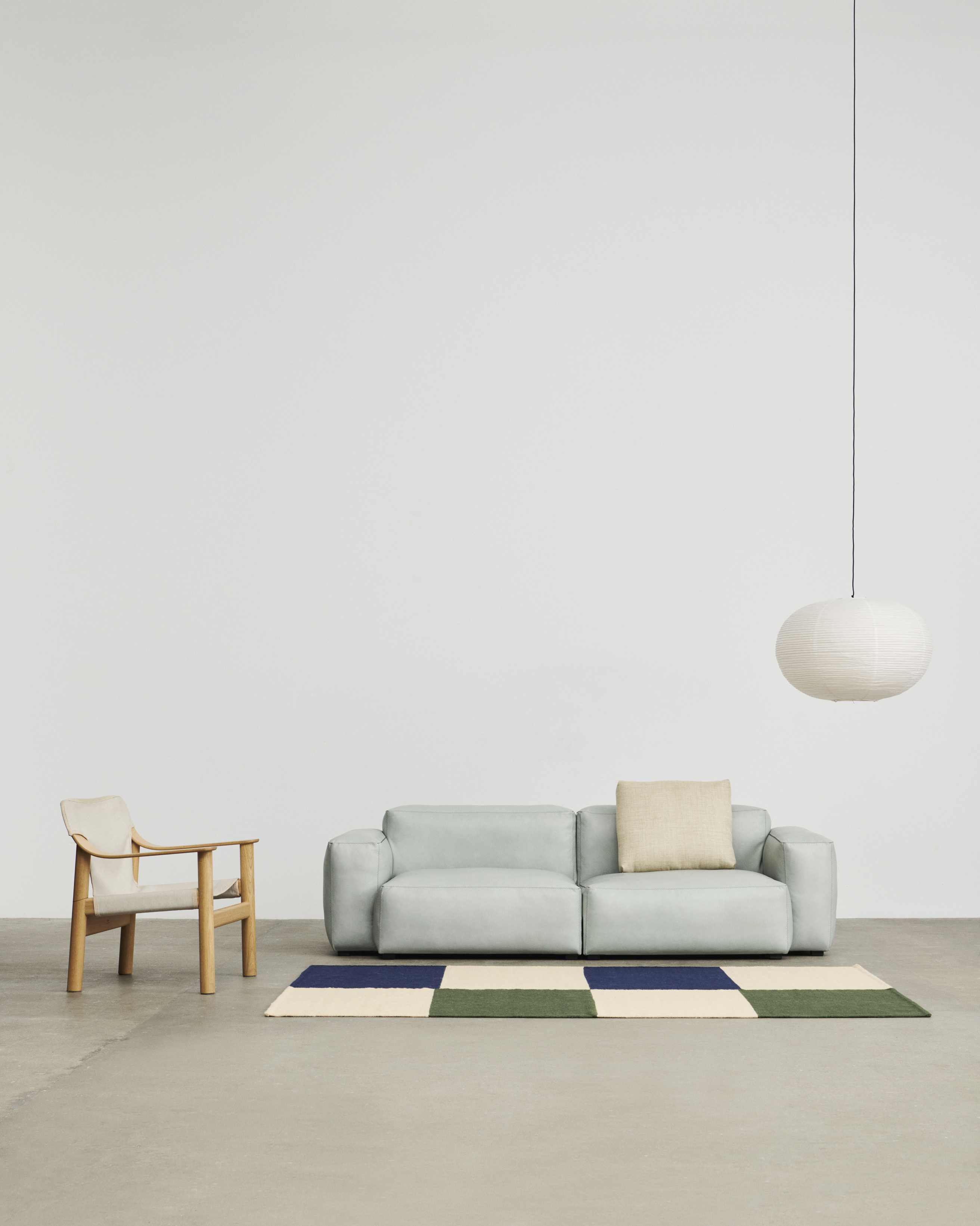 Mags Soft Sofa in hellem Blau mit beigem Kissen und Teppich im minimalistischen Wohnzimmer.