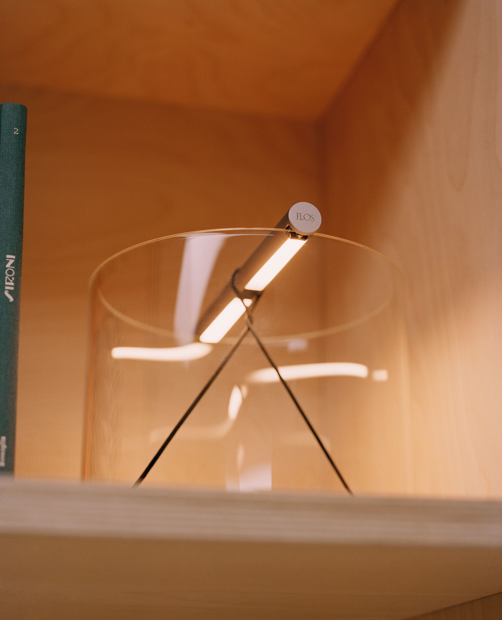 To-Tie T3 LED Tischleuchte von Flos, schwarz eloxiert, mit transparentem Glaszylinder im Regal.