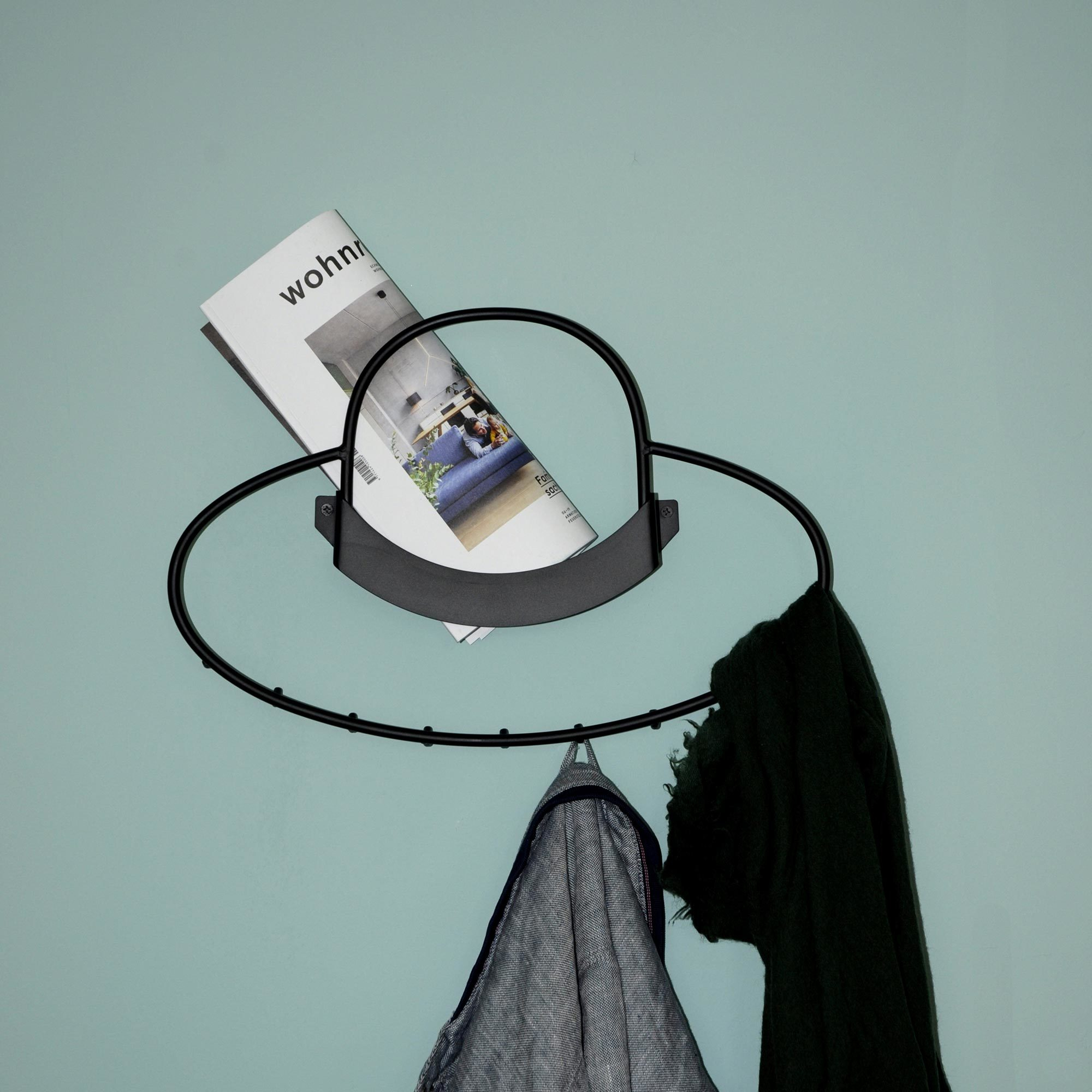Schwarze Hat Wandgarderobe mit Haken, Jacke, Schal und Magazin an hellblauer Wand.