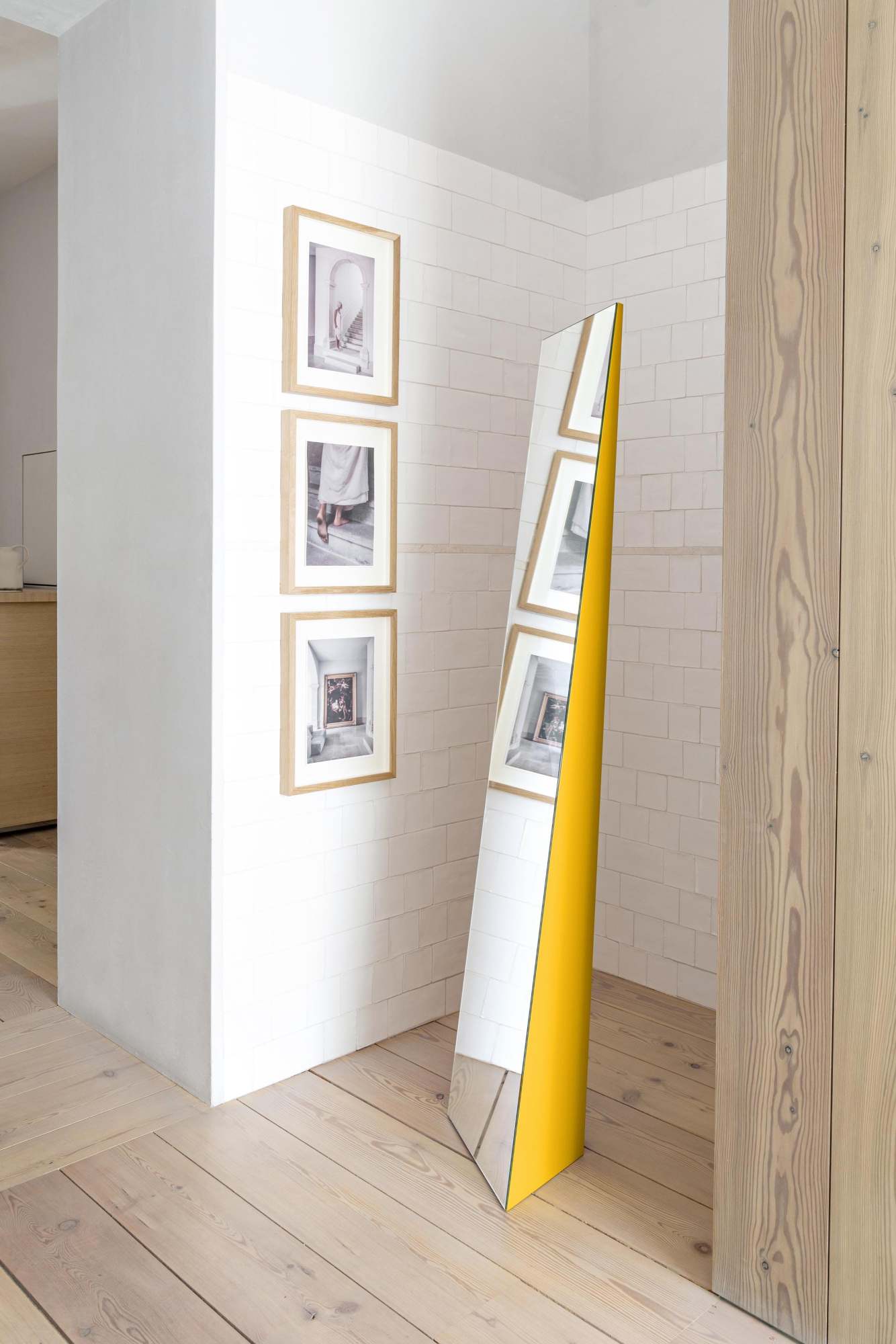 Schönbuch Beam Standspiegel: Gelber, dreieckiger Spiegel im Flur, der Bilder an der Wand reflektiert. Moderner Designspiegel.