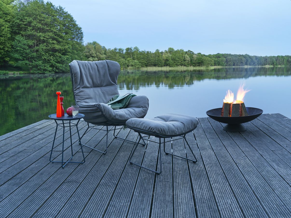 Leyasol Ottoman Outdoor von Freifrau Manufaktur: Grauer Sessel und Hocker am See mit Feuerstelle.
