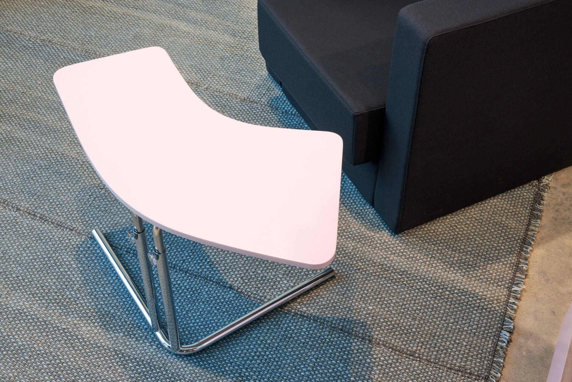 K26L Tecta Beistelltisch mit rosa Tischplatte und verchromtem Stahlrohrgestell neben einem schwarzen Sofa.