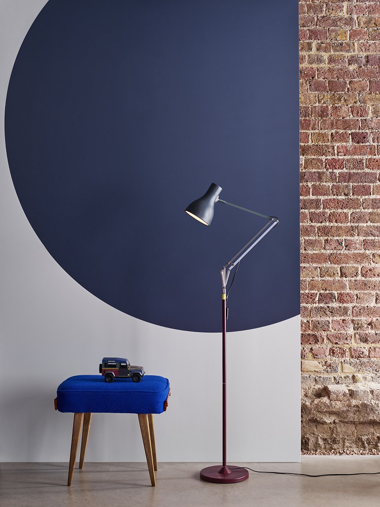 Moderne Stehlampe mit verstellbarem Arm, blauer Hocker mit Spielzeugauto vor Wand mit Farbkreis.