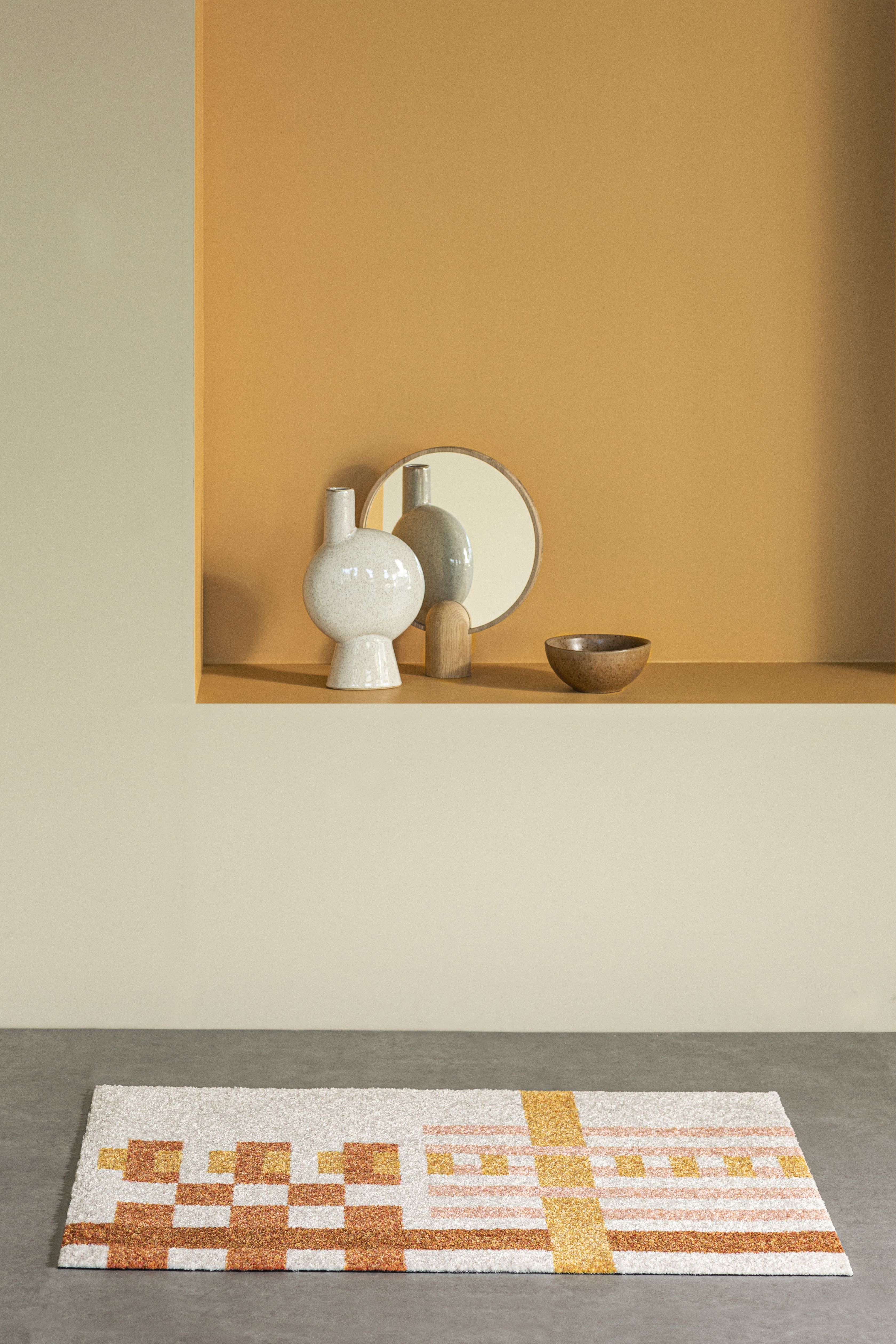 Nahaufnahme der Loom Fußmatte von Heymat mit geometrischem Muster in warmen Farben.