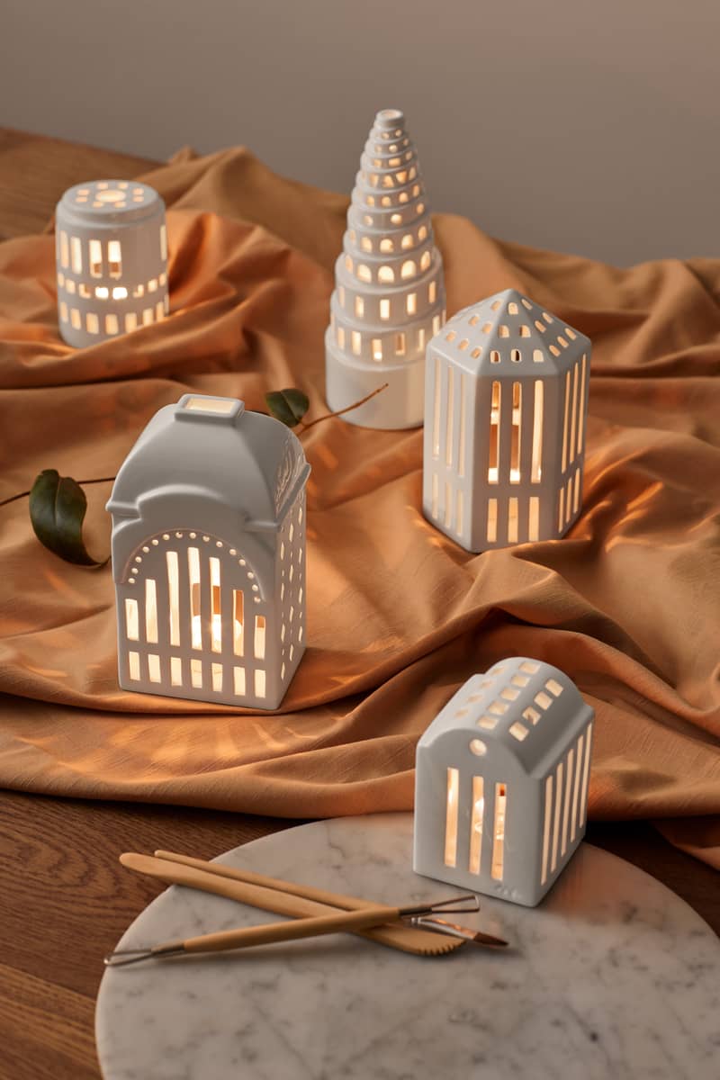 Verschiedene weiße Urbania Lichthäuser von Kähler, darunter ein kleiner Turm, auf einem goldenen Tuch und Marmortablett.