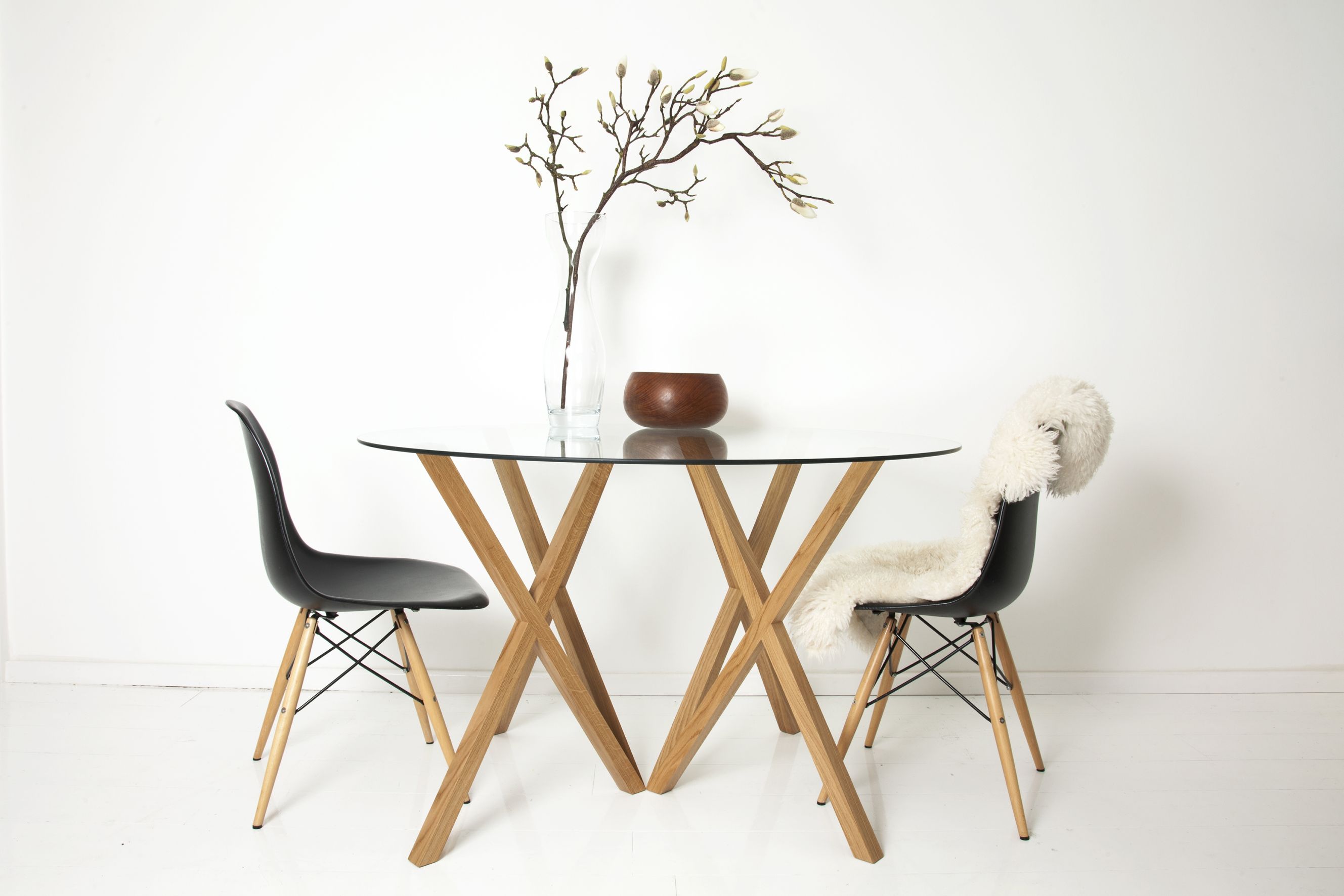 Runder Glastisch mit Holzgestell und zwei schwarzen Stühlen, einer mit Schaffellauflage.