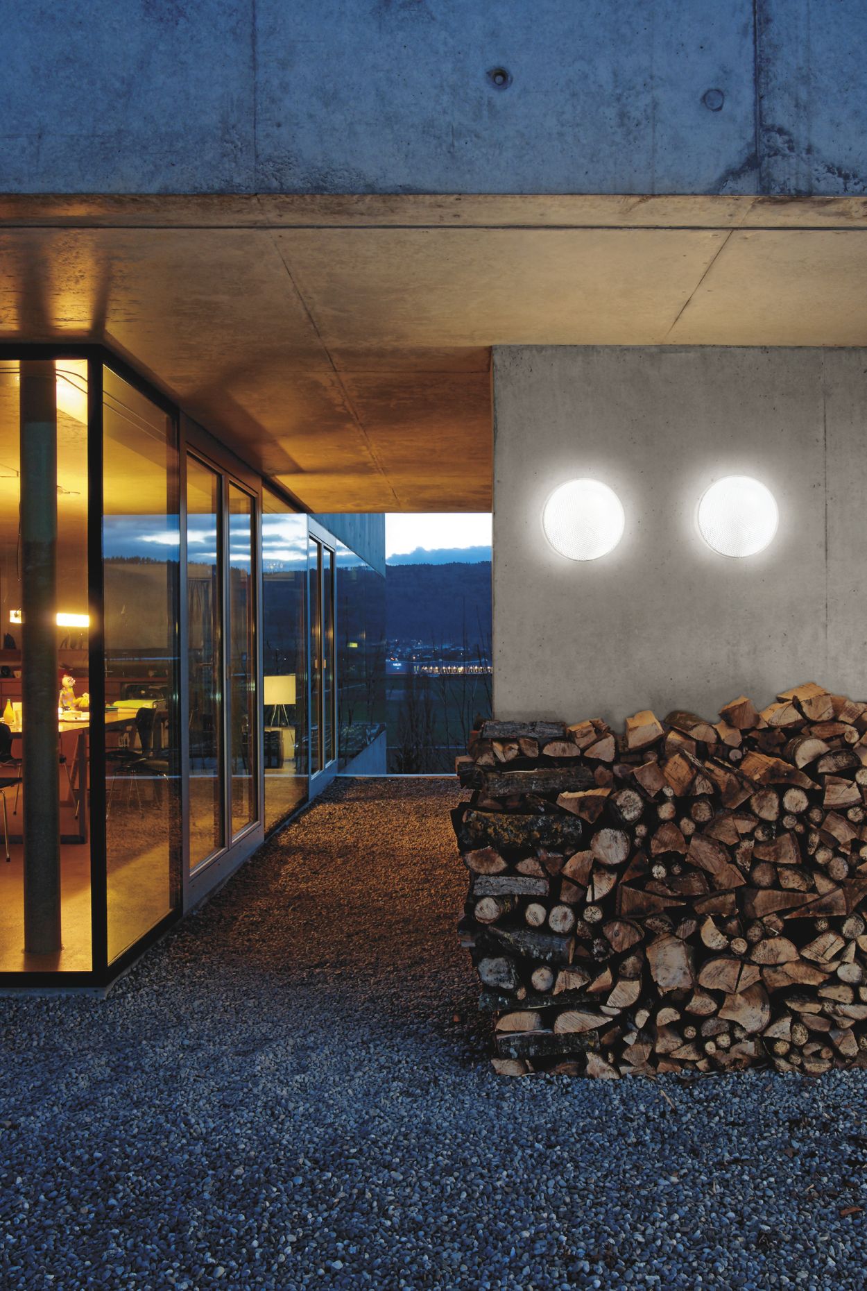 Zwei runde Belux O-lite Wandleuchten an Betonwand über Holzstapel, Außenbeleuchtung für Haus.