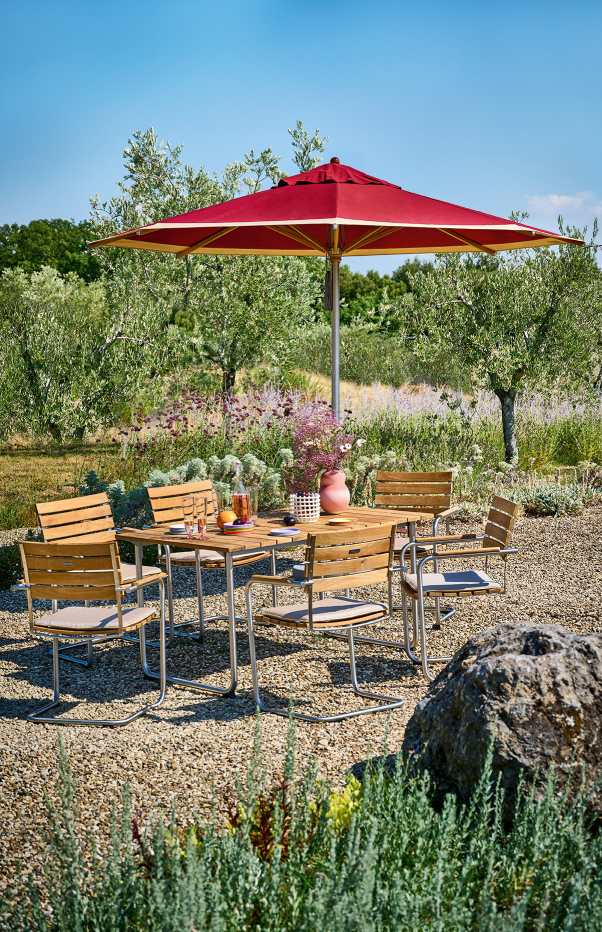 Weishäupl Trend Sonnenschirm in Rot über einer Gartengarnitur mit Holztisch und Stühlen im Freien.