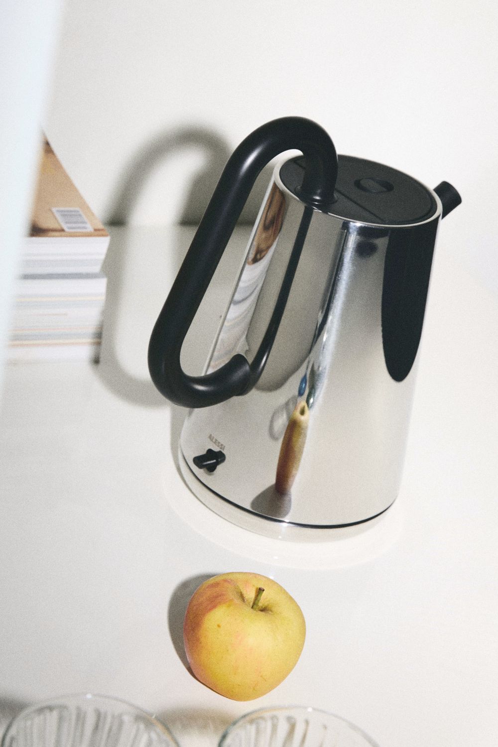 Alessi Wasserkocher NE01 B Toru aus Edelstahl mit schwarzem Griff und Apfel.