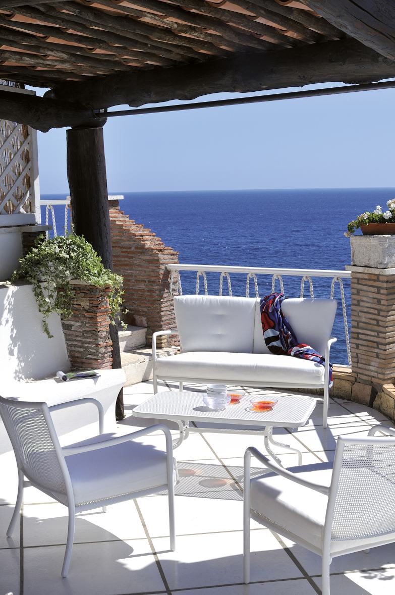 Weißer Athena Couchtisch von Emu Outdoor mit Stühlen und Sofa auf einer Terrasse mit Meerblick.