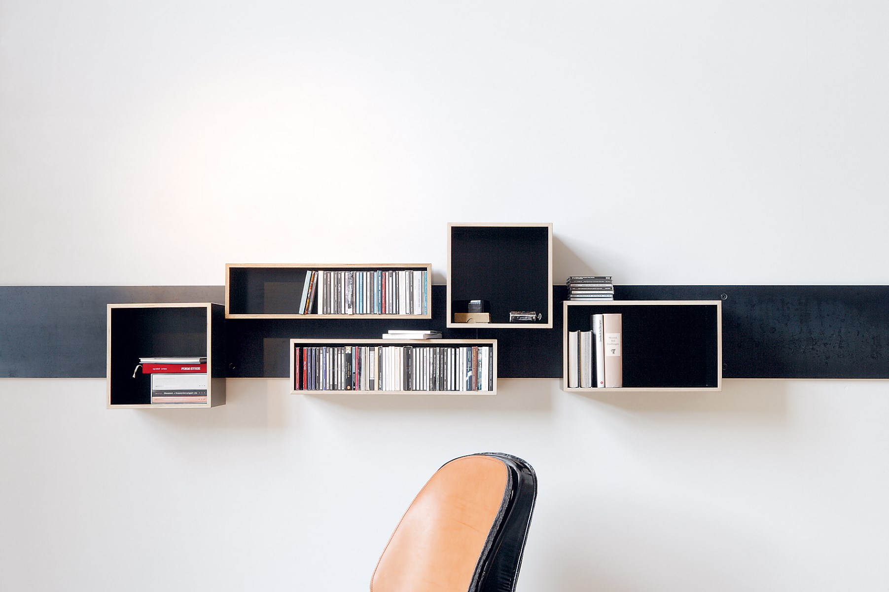 Magnetique Regal von Nils Holger Moormann an weißer Wand mit Büchern und CDs.