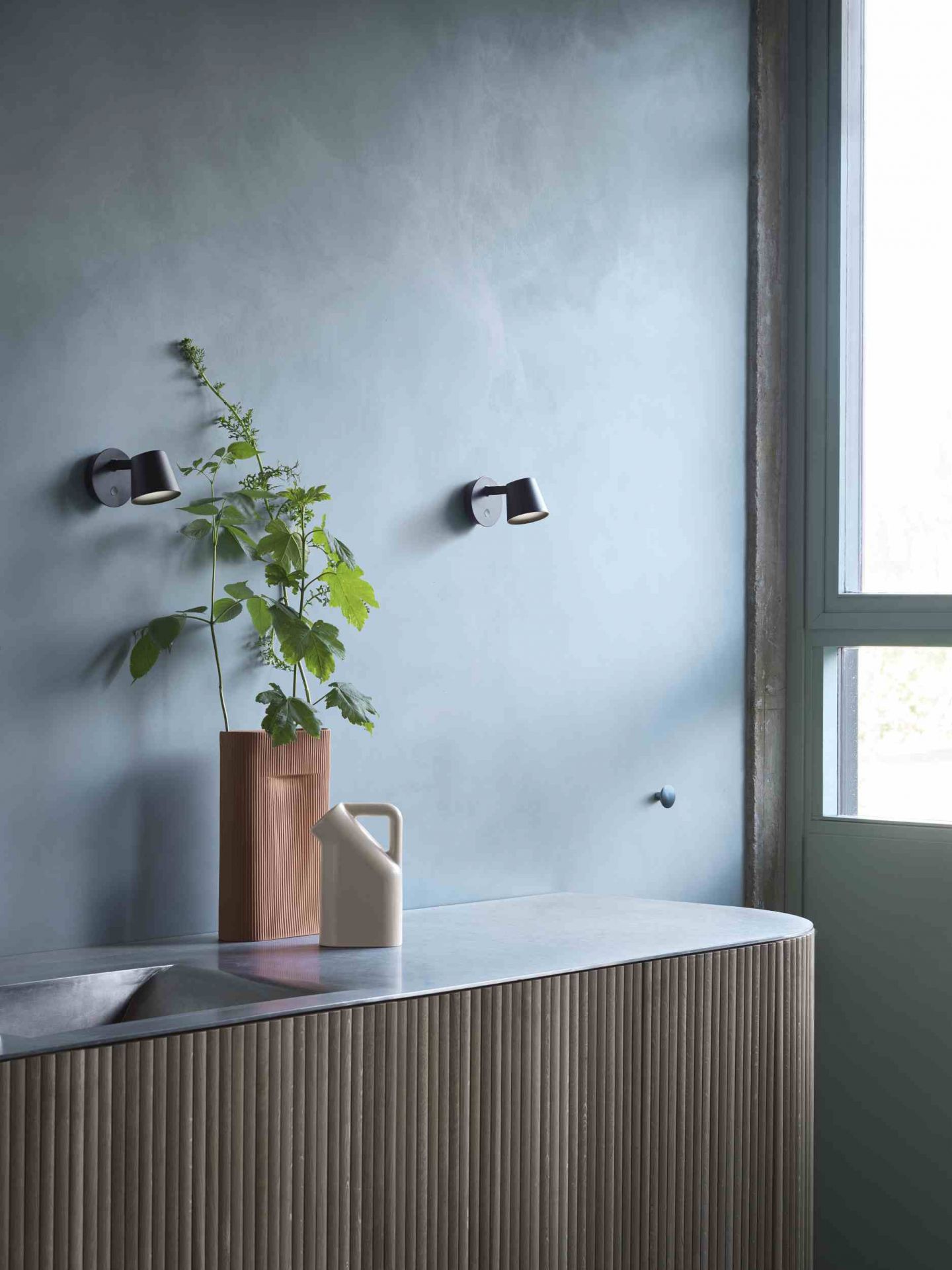 Nahaufnahme von zwei weißen Muuto Tip Wandleuchten, die an einer blauen Wand über einem Waschtisch montiert sind.