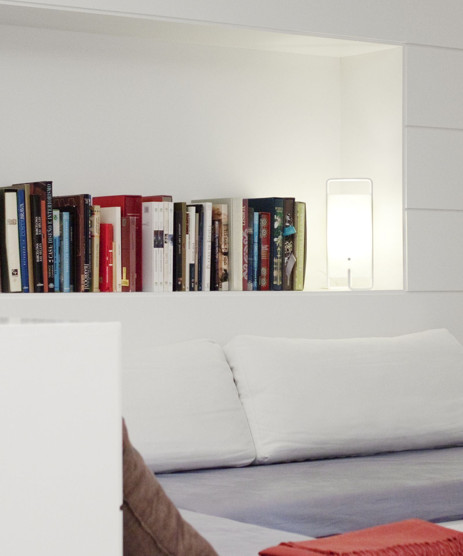 Weiße ASA Tischleuchte Santa & Cole neben Büchern in einem weißen Regal.