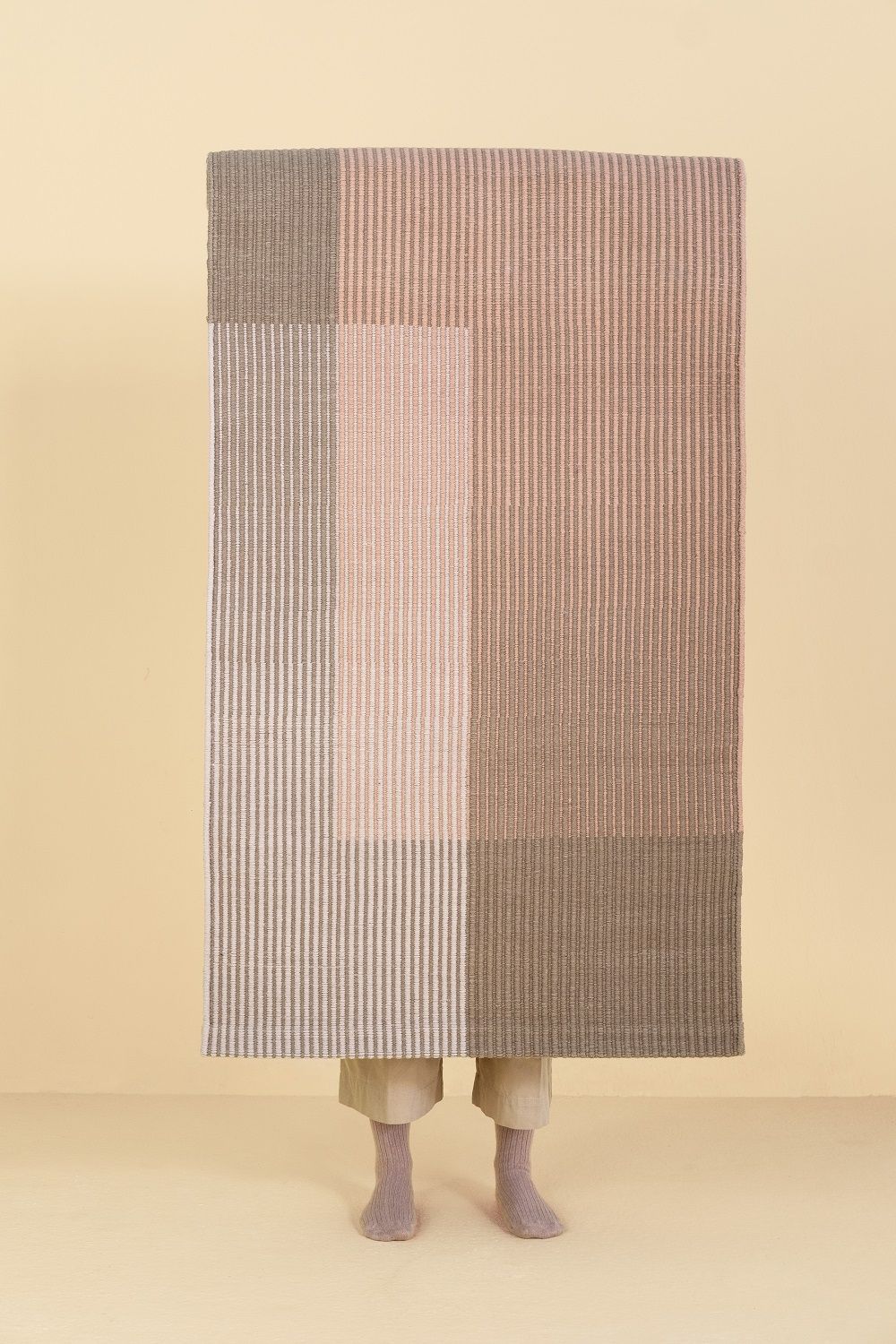 Nanimarquina Haze Rug Teppich mit vertikalen Streifen in Rosa- und Brauntönen, verdeckt eine Person.