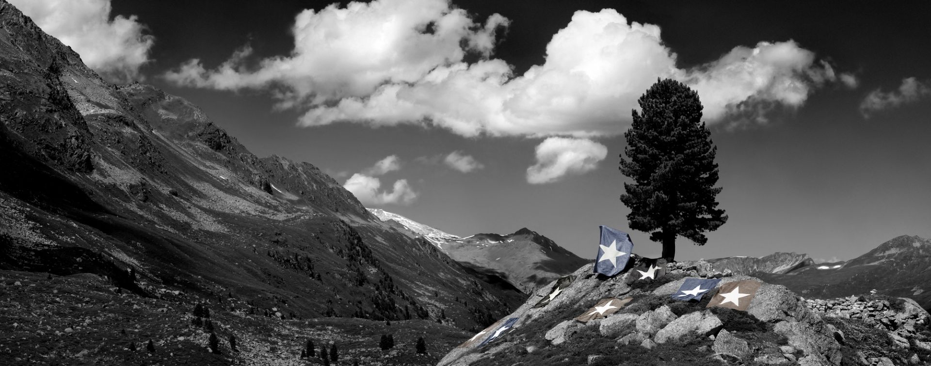Schwarz-Weiß-Foto einer Berglandschaft mit verstreuten Flaggen, die einen weißen Stern auf blauem Grund zeigen.