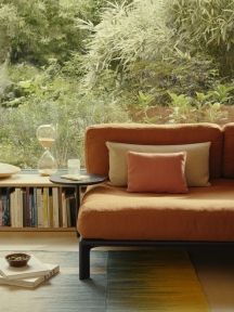 Orangefarbenes Sofa mit beigen und roten Vitra Kissen vor Fenster mit Gartenblick. Dekorative Sofakissen für Wohnzimmer.