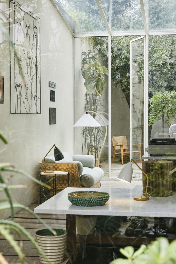 Helle, moderne Inneneinrichtung mit Gubi Timberline Stehleuchte, Tischleuchten, Kunstwerken und Pflanzen in einem Wintergarten.