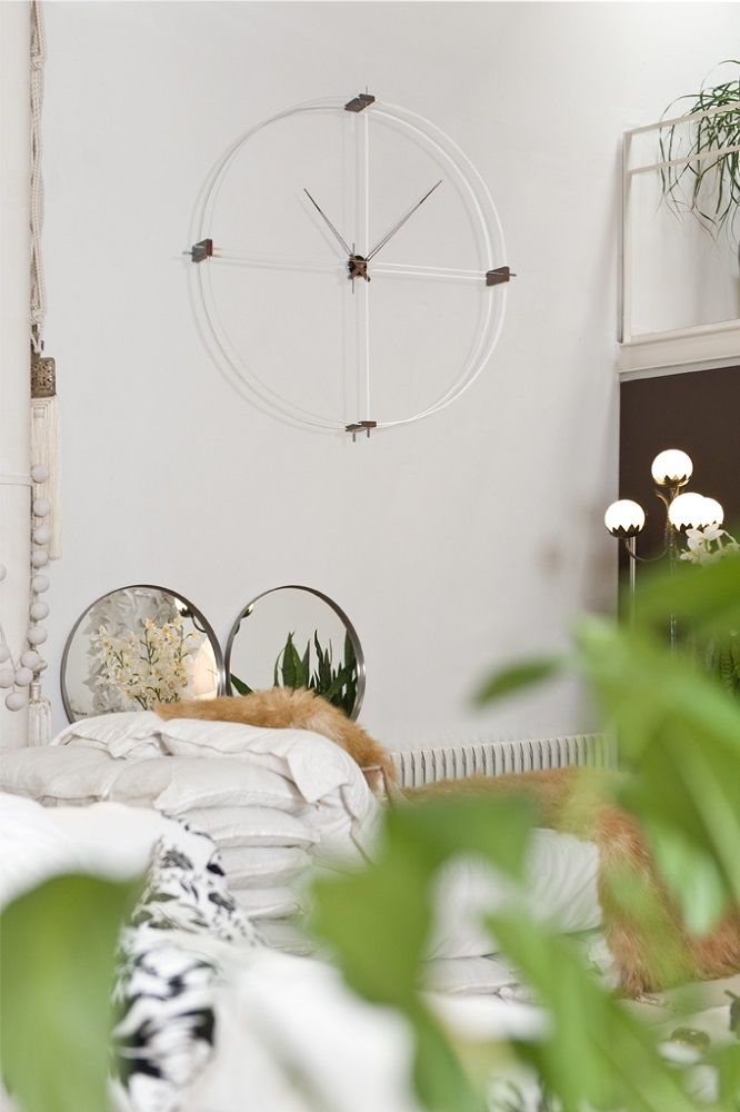 Delmori Clock Wanduhr in Weiß/Chrom an einer weißen Wand über einem Bett. Moderne Wanddekoration.