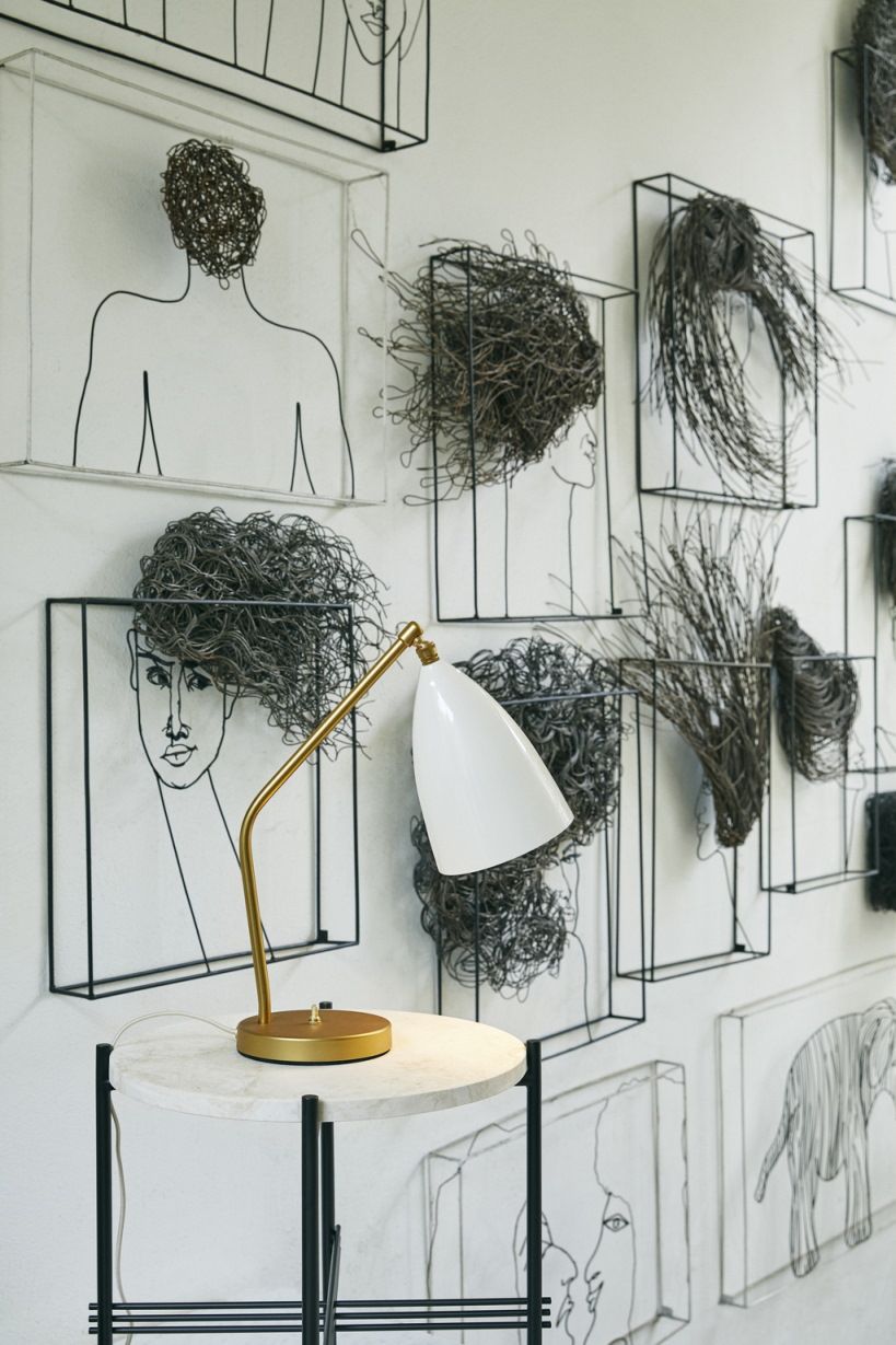 Gräshoppa Tischleuchte von Gubi, alabasterweiß glänzend, auf einem Beistelltisch vor einer Wand mit Kunst.