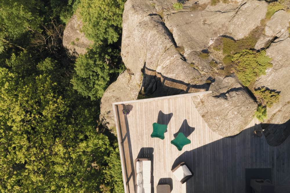 Draufsicht: Mariposa Outdoor Butterfly Chair Sessel in Waldgrün auf Holzterrasse mit Felsen und Bäumen.