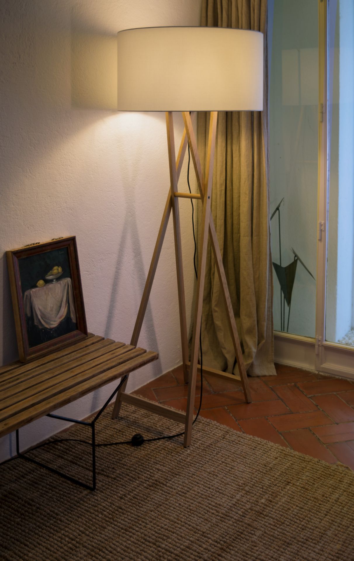 Cala Stehleuchte von Marset mit Holzgestell und hellem Lampenschirm neben Bank.