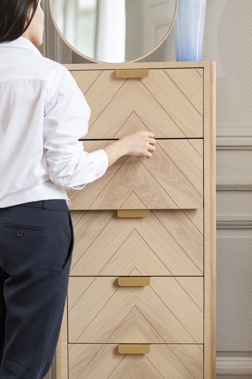 Frau öffnet Schublade der Marius Chiffonier Kommode von Hartô. Holzkommode mit Fischgrätmuster und goldenen Griffen.