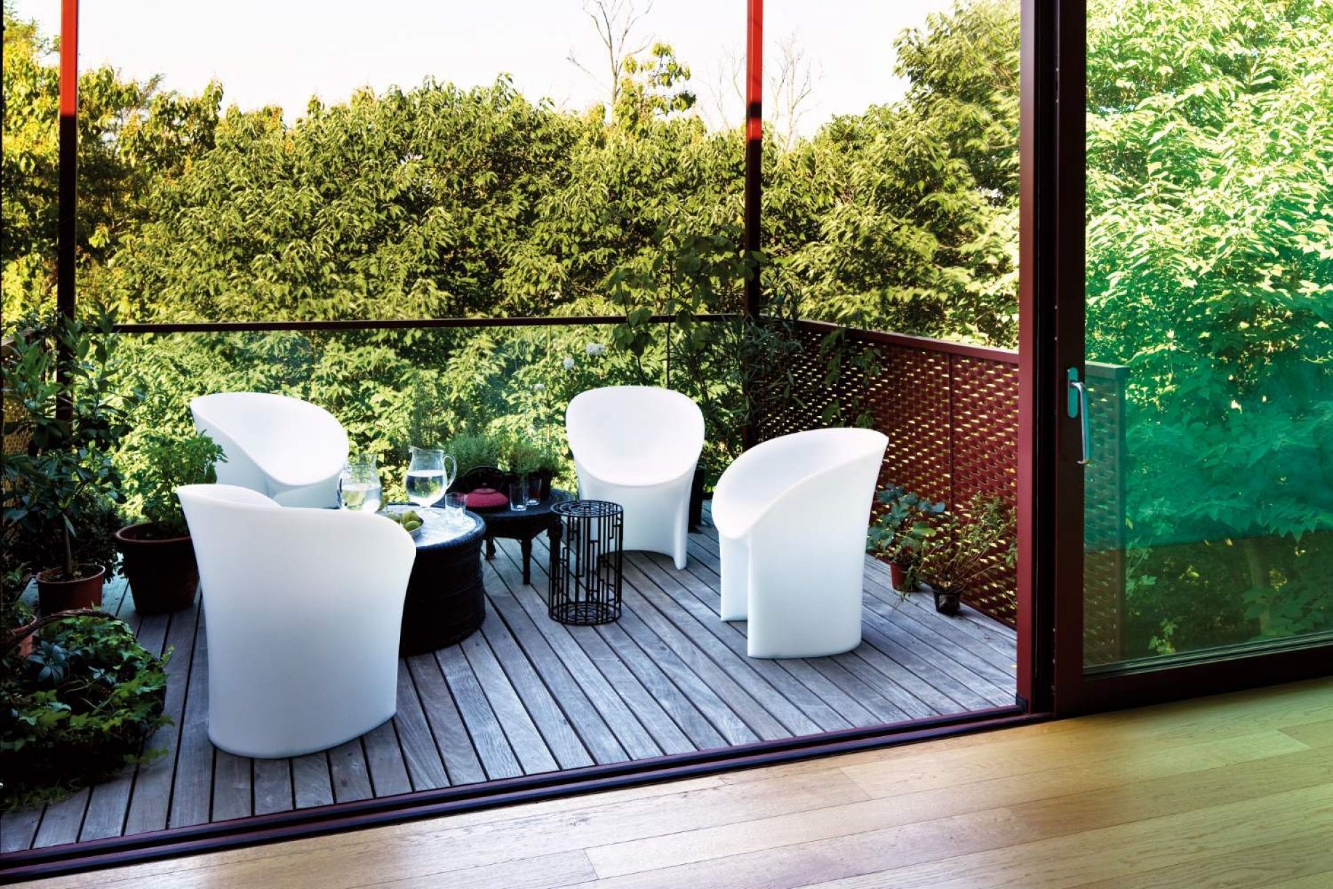 Vier weiße Moon Sessel von Moroso auf einer Holzterrasse mit Pflanzen und Tisch.