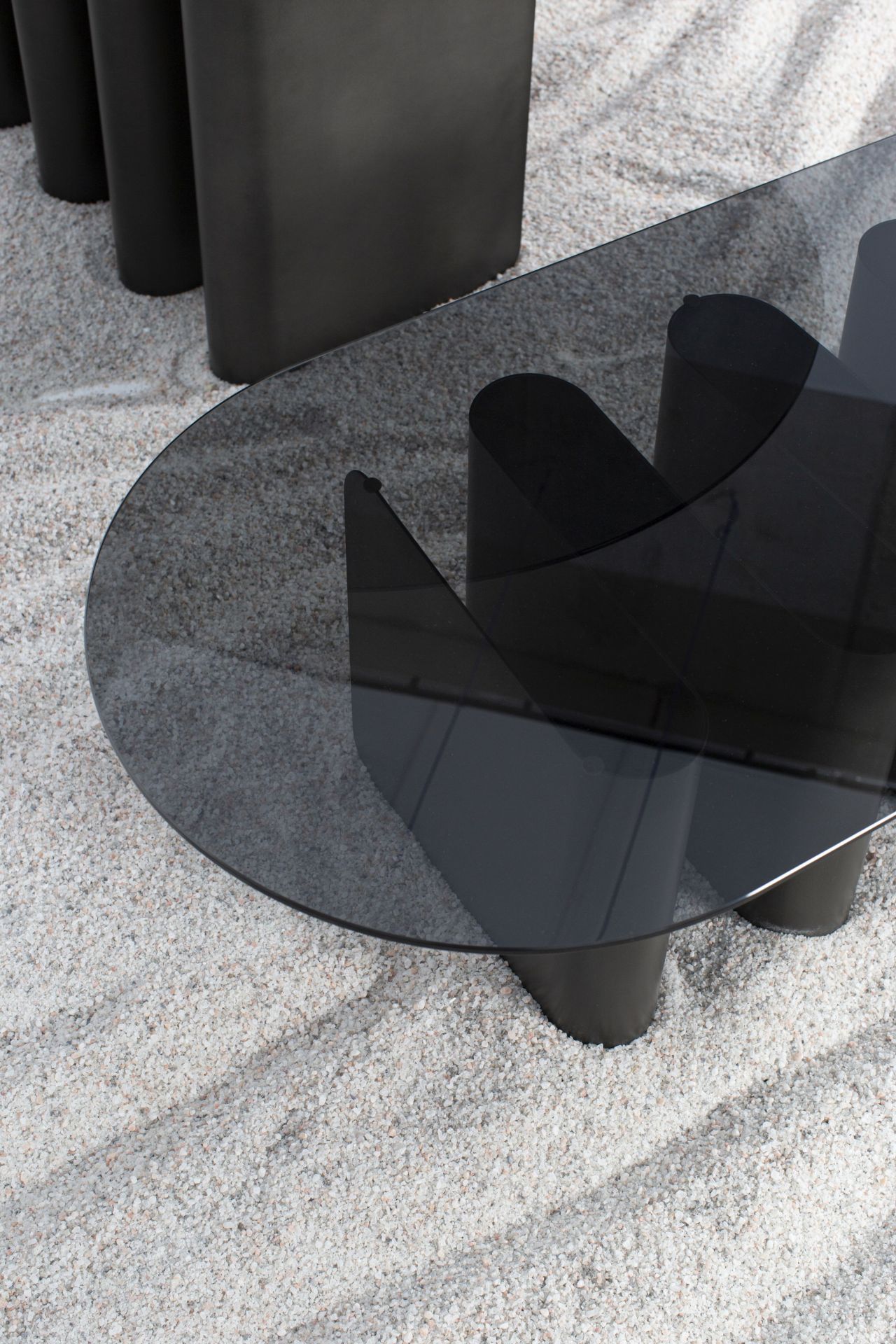 Nahaufnahme des modernen Tavolino2 Beistelltisches von Pulpo mit ovaler Glasplatte und schwarzen Beinen auf Kies.
