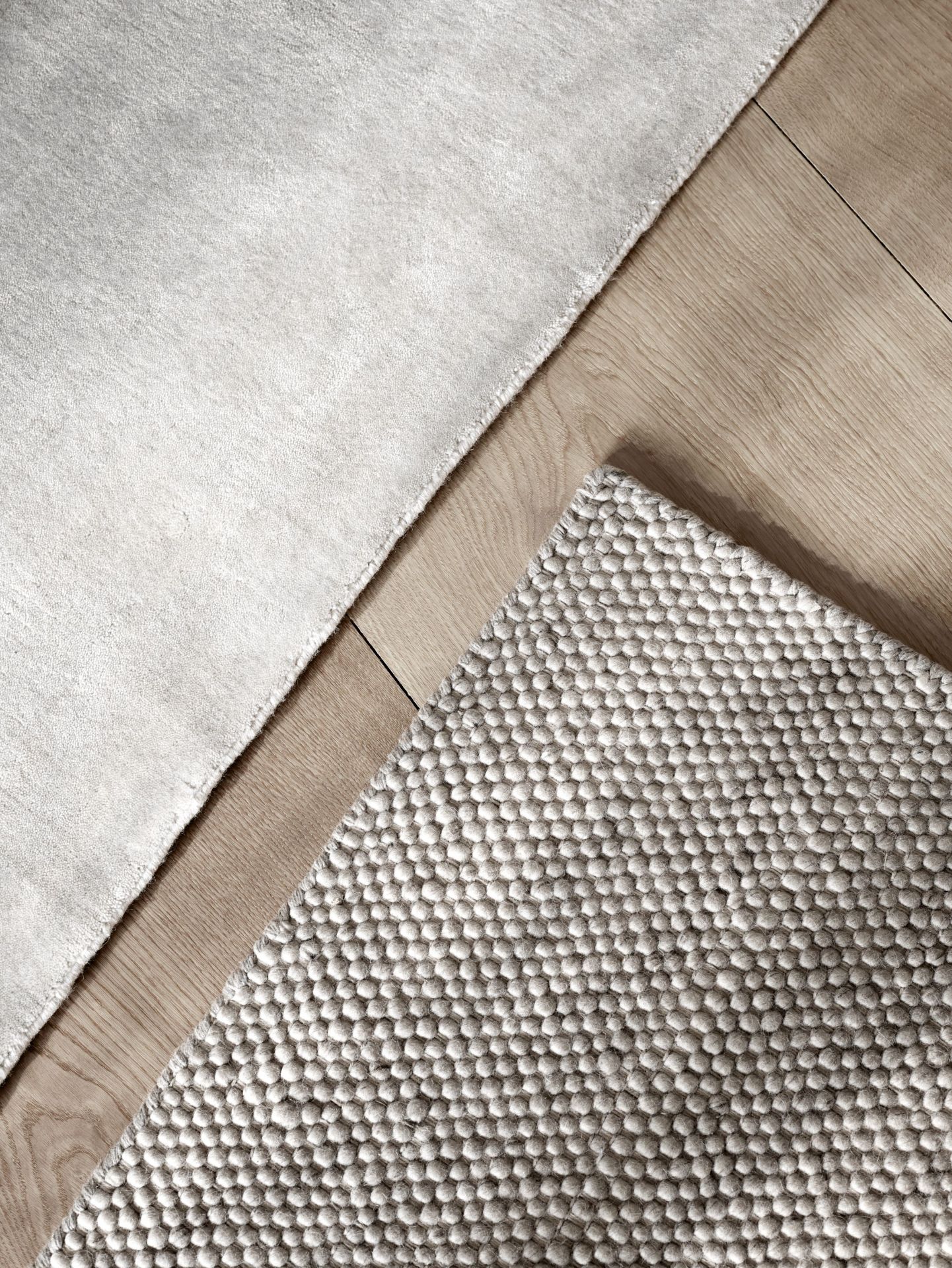 Detailaufnahme von zwei Vipp Teppichen auf Holzboden, ein Wollteppich und ein Teppich mit Noppenstruktur.