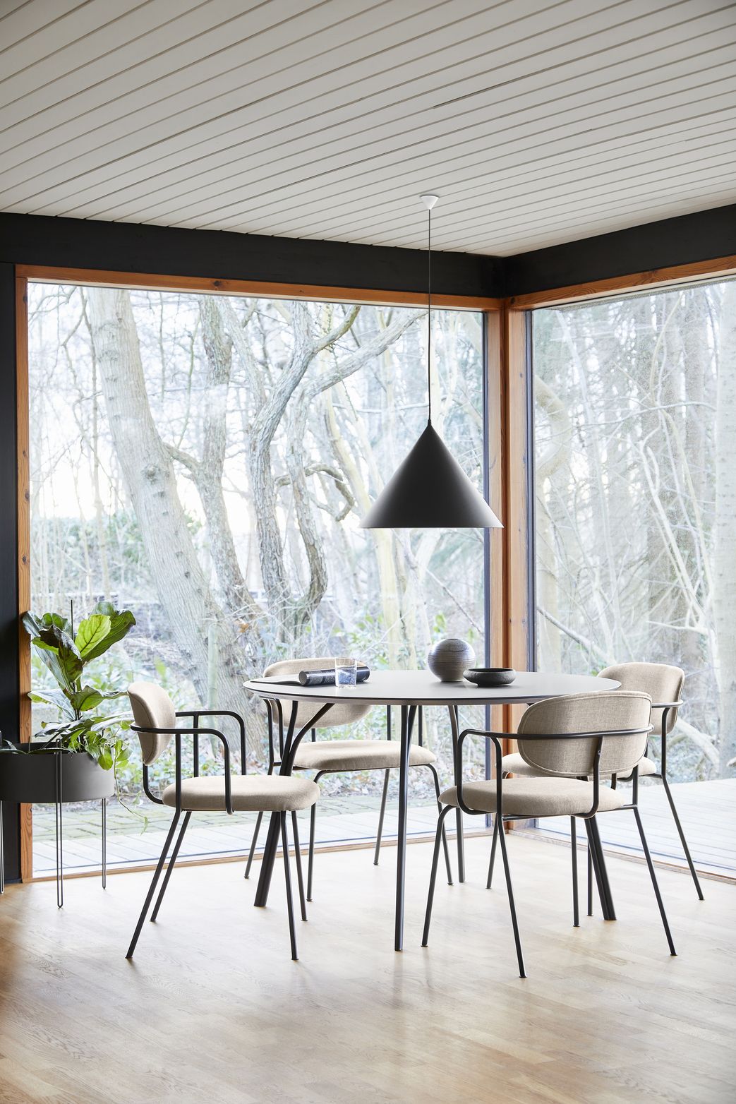 Schwarze Annular Pendelleuchte von Woud über Esstisch in modernem Esszimmer mit großem Fenster.