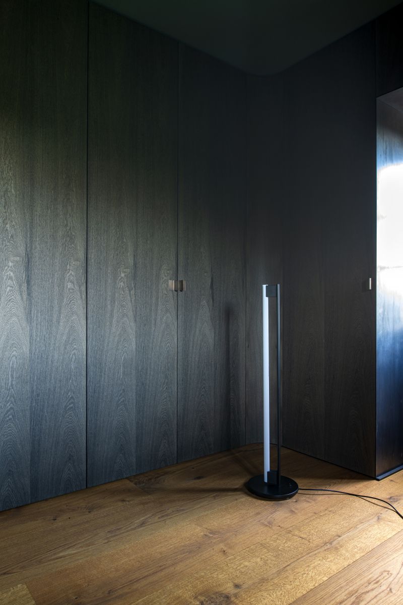 Schwarze Tube Light Stehleuchte von ClassiCon im modernen Interieur mit dunklen Holzschränken und Holzboden.