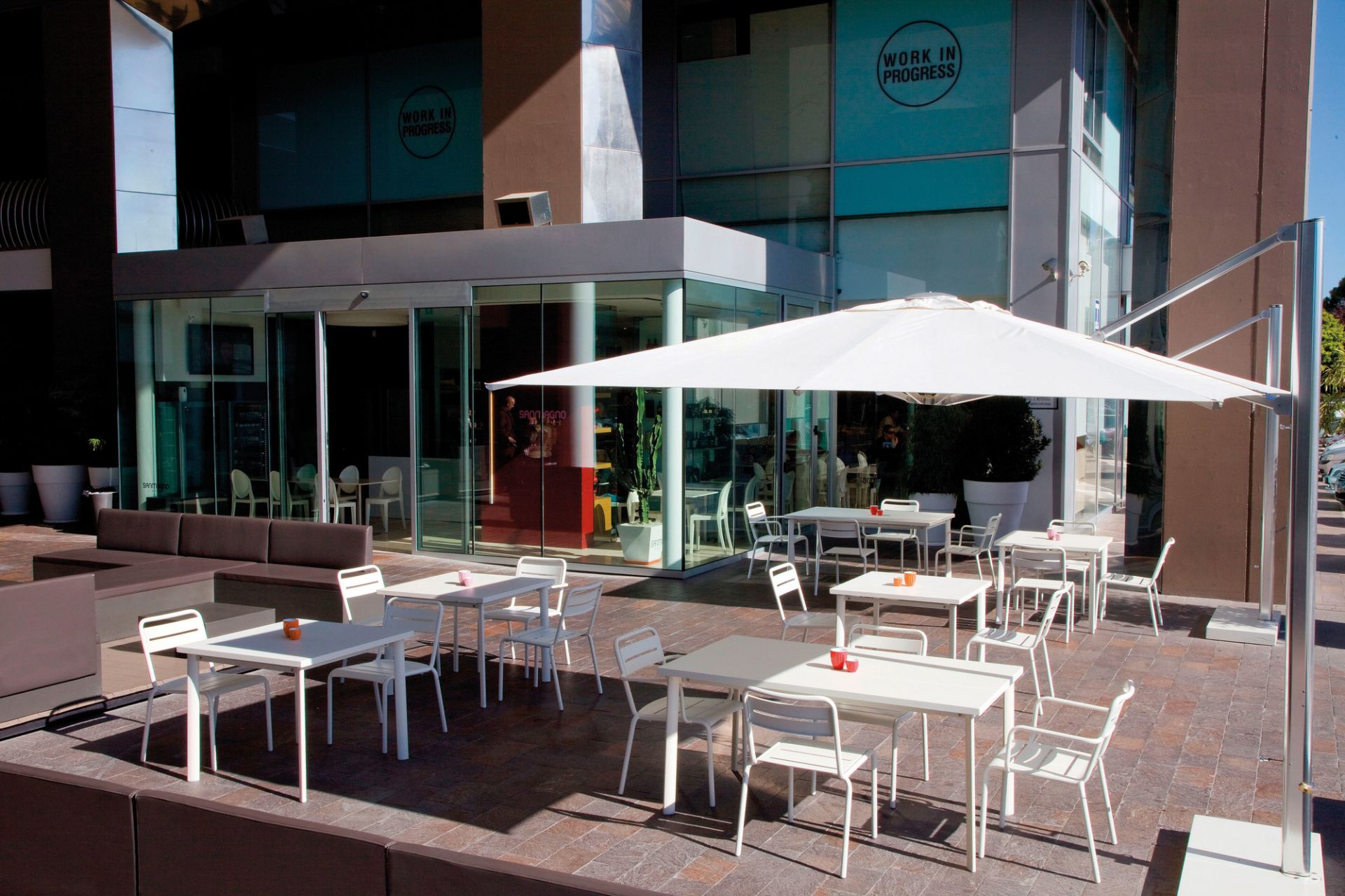 Außenbereich mit weißen Emu Armlehnstühlen und Tischen unter einem Sonnenschirm, modernes Design.