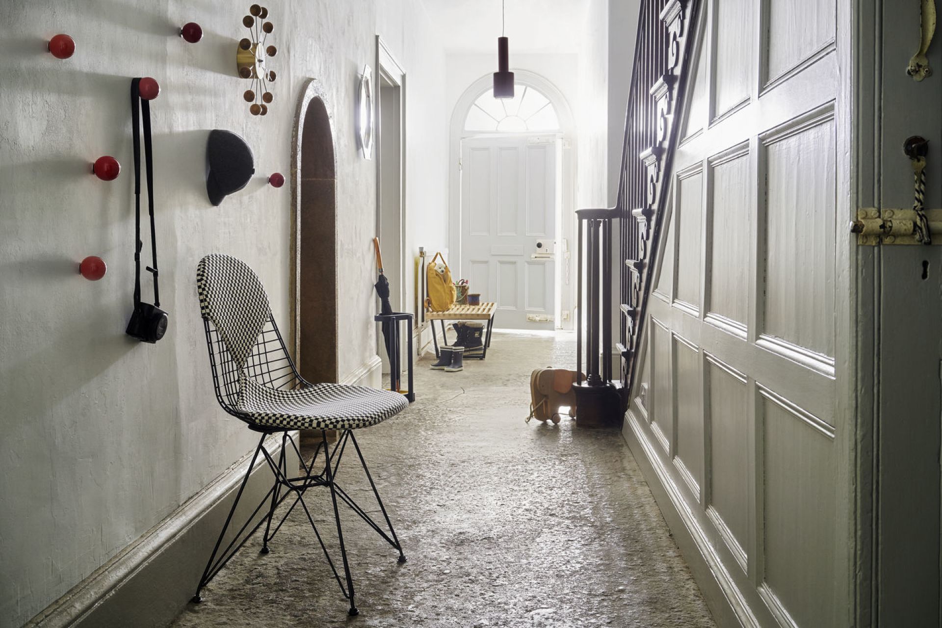 Flur-Szene mit roten Coat Dots Garderobenhaken von Vitra an der Wand, daneben eine Design-Sitzgelegenheit.