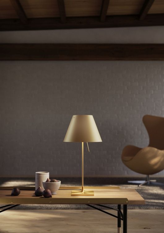 Costanzina Tischleuchte aus Messing von Luceplan: Elegante, goldfarbene Lampe auf einem Holztisch mit Feigen.