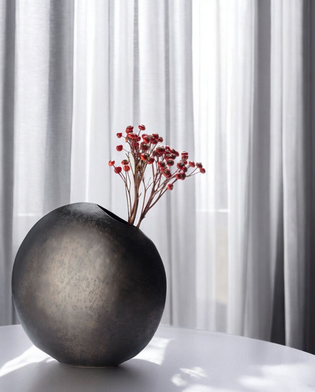 Monrovia Vase: Runde, dunkle Design-Vase mit roten Beeren-Zweigen als Dekoration. Einzigartiges Deko-Objekt.