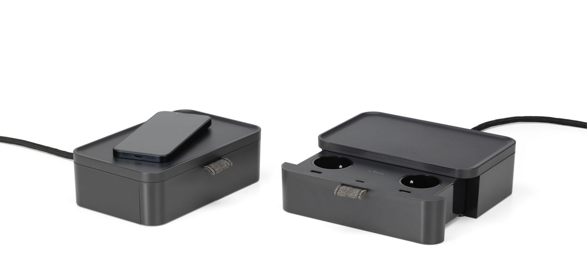 Ampi Wireless Charger und Vitra Mehrfachsteckdose Basic dark mit Smartphone zum kabellosen Laden.