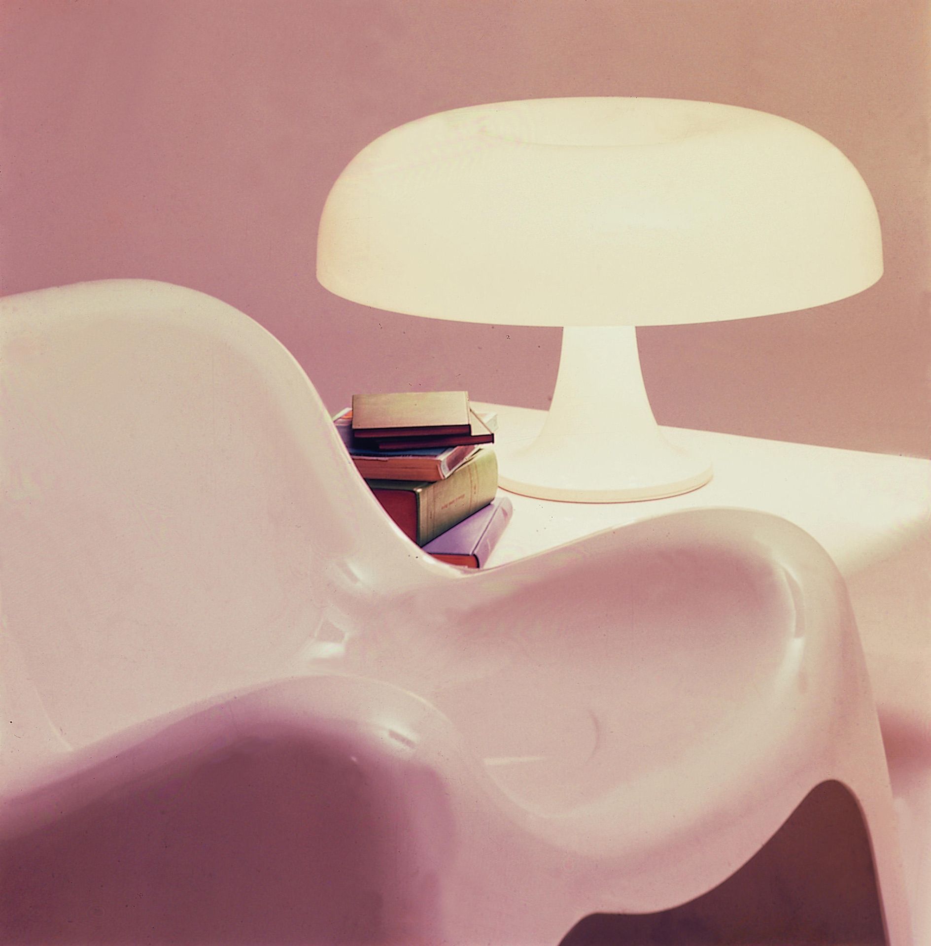 Nesso Tischleuchte von Artemide neben einem Stapel Bücher auf einem weißen Tisch.