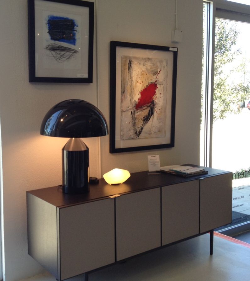 Atollo Lampe von Oluce, schwarzes Aluminium, auf einem Sideboard mit Kunstwerken im Hintergrund.