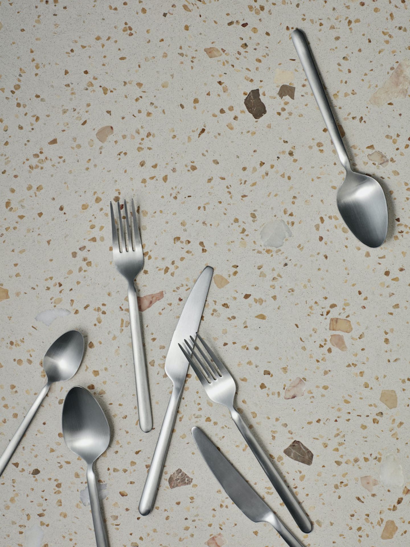 Stella Besteck-Set: Silbernes Besteck, Messer, Gabeln, Löffel auf gemustertem Untergrund. Hochwertiges, modernes Besteck für stilvolle Tischdekoration.